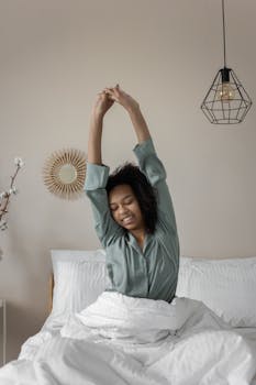 African American woman waking up, stretching arms in cozy bedroom setting.