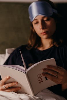 Woman reading a book in bed with a sleep mask, capturing a cozy nighttime vibe.